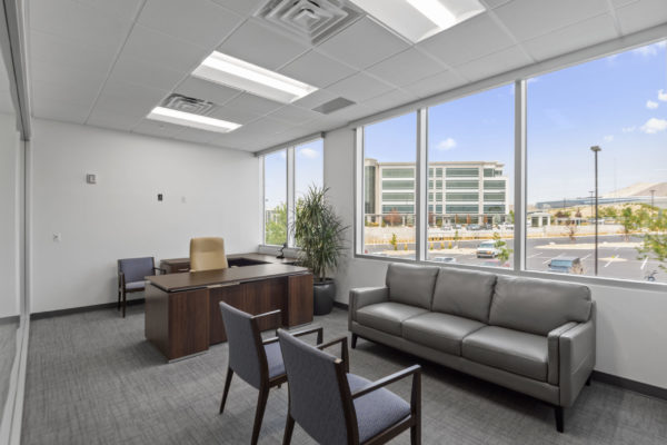 Large office with couch, chairs, desk, and a wall of windows | Utah Commercial Real Estate
